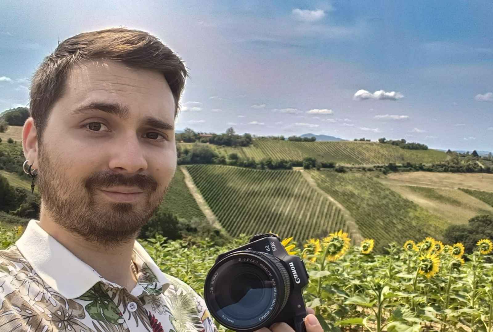 Paul con fotocamera in mano in un campo di girasoli sulle colline