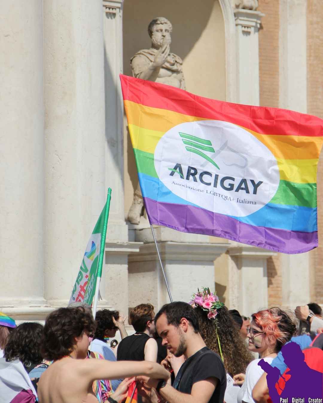 Manifestanti con una bandiera di arcigay con dietro una statua in Piazza Roma a Modena
