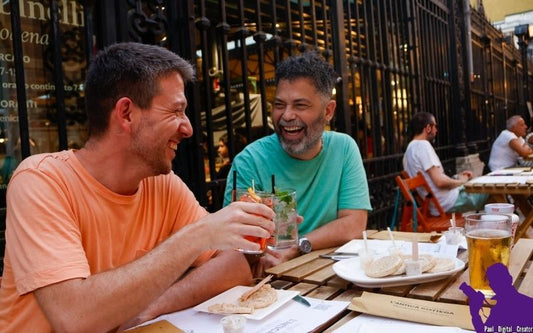 un modello vestito di arancione con spritz in mano brinda con modello vestito verde con in mano mojito