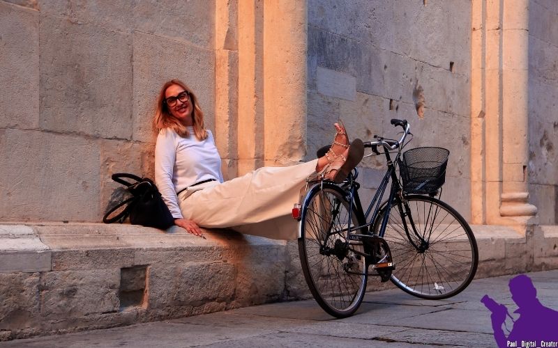 modella seduta vicino alla parete del Duomo di Modena che poggia i piedi su una bici nera sorridendo